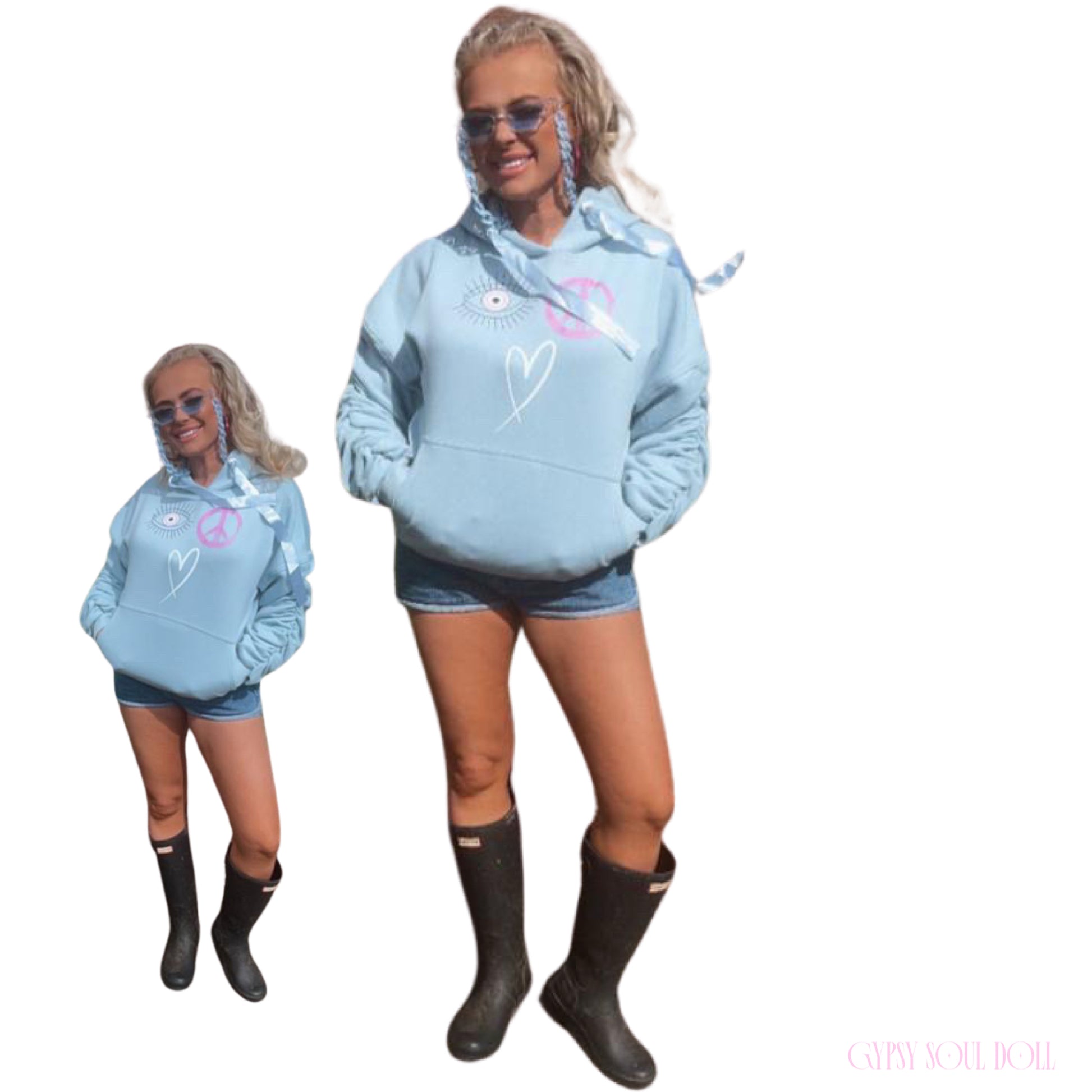 A dual-pose studio mockup of a blonde model showcasing the Gypsy Soul Doll baby blue graphic oversized street-style hoodie featuring pink and white evil eye, peace sign, and heart doodles, styled with denim shorts and black hunter festival wellington boots.
