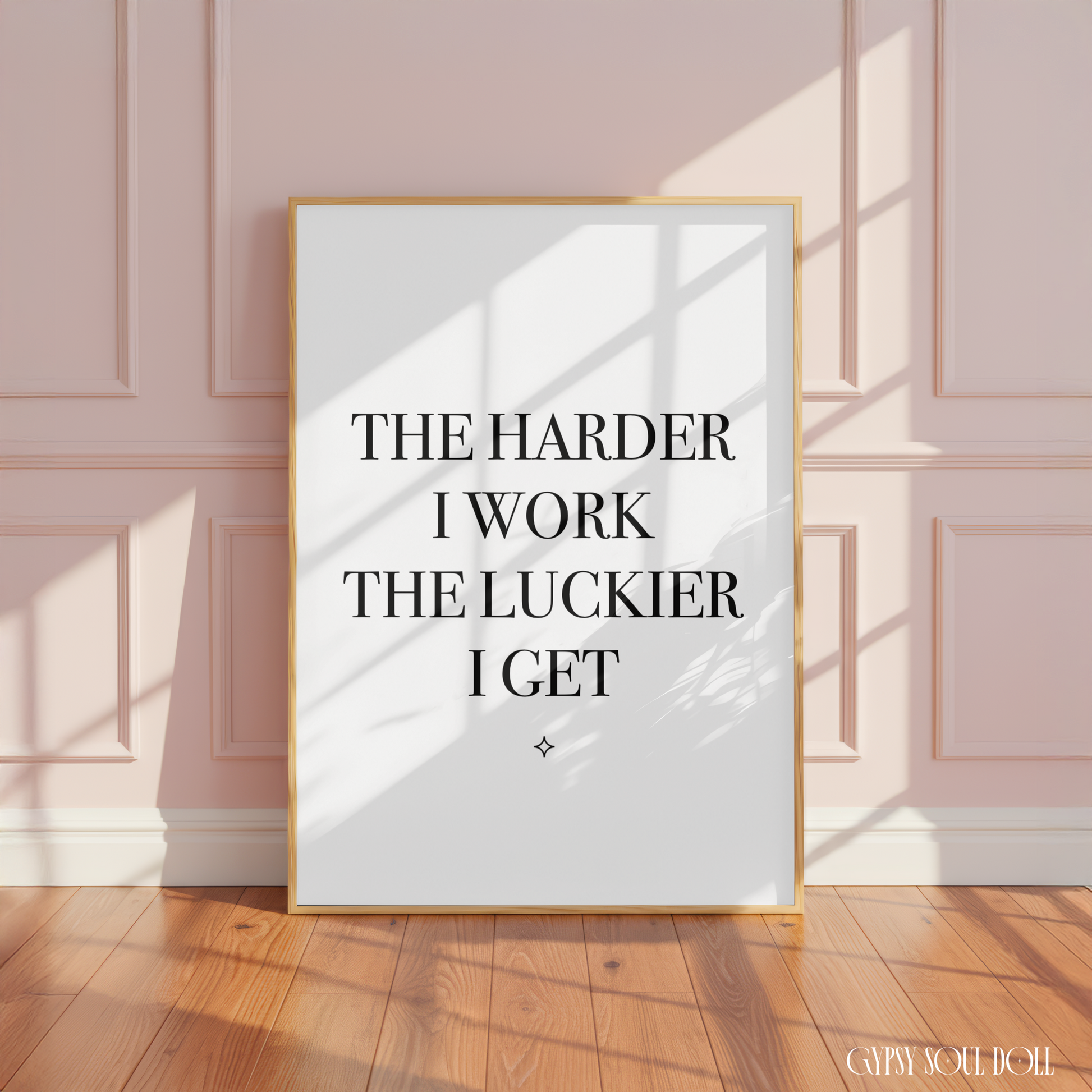 Minimalist black and white manifestation affirmation typography print reading The Harder
I Work The Luckier I Get with a tiny star accent in a large oak frame leaning against a panelled pink wall.
