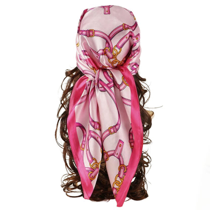 A pink silk classy scarf with a gold and magenta horsebit pattern, styled on a mannequin head with dark brown wavy hair against a plain white background.