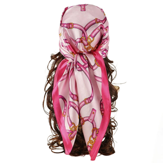 A pink silk classy scarf with a gold and magenta horsebit pattern, styled on a mannequin head with dark brown wavy hair against a plain white background.