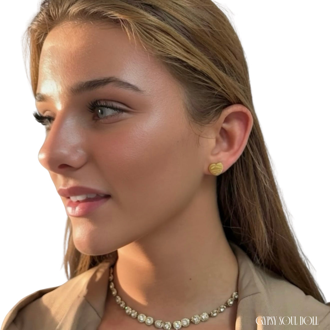 A close-up side profile of a woman wearing a small round gold stud earring and a matching gold necklace with clear stones, against a clean white background.