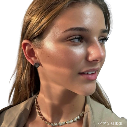 Close-up of a woman wearing a small gold heart-shaped fashion stud earring and a beaded necklace, shown against a plain white background.