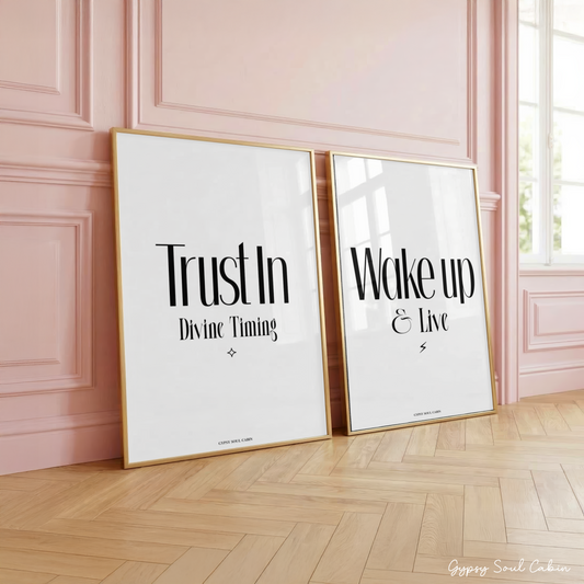 Set of two minimalist black and white typography prints featuring inspirational daily reminder quotes, leaning in gold frames on a wooden herringbone floor against a pink panelled wall.
