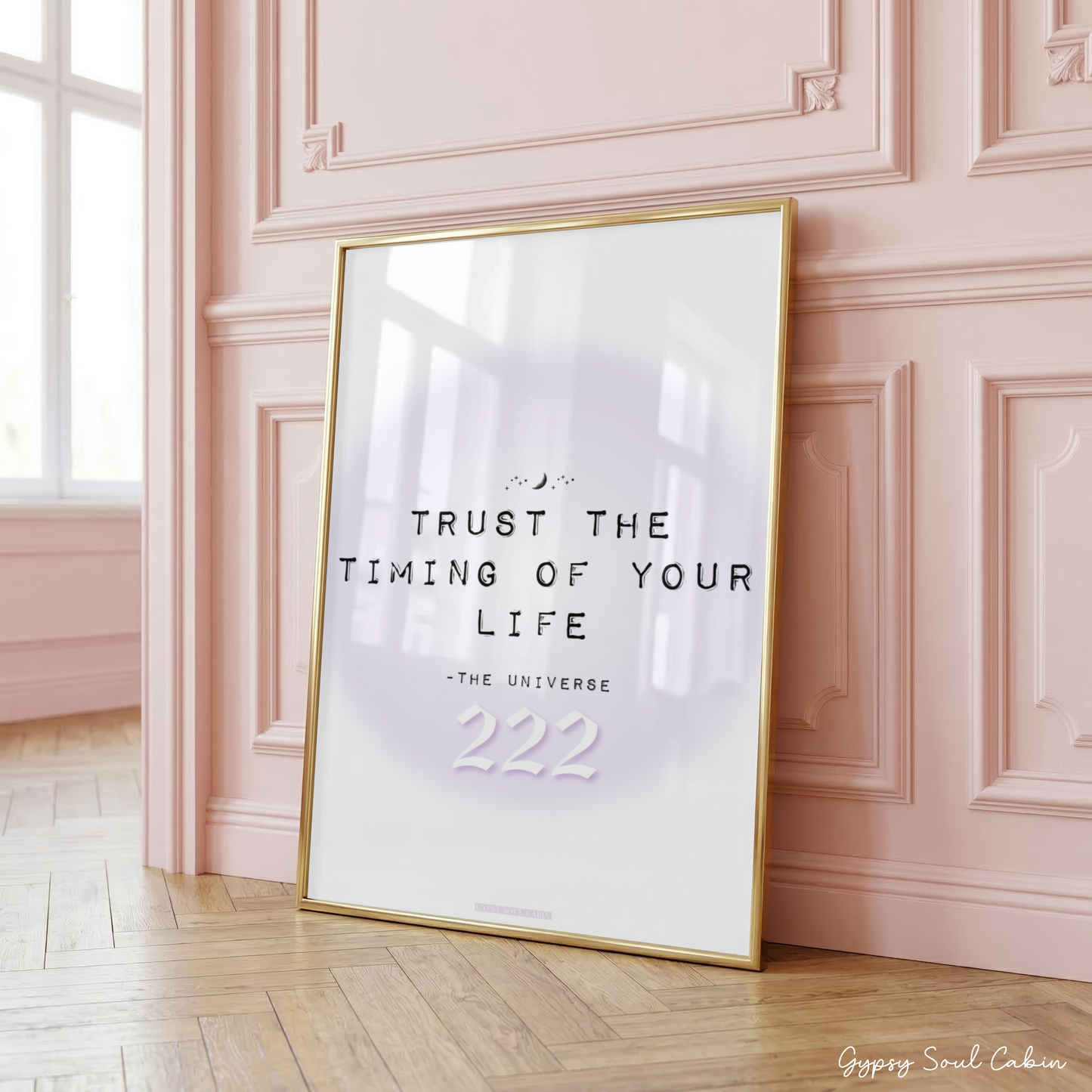 Minimalist purple gradient aura typography print reading Trust The Timing Of Your Life 222 in a large gold frame leaning against a classic panelled pink wall.