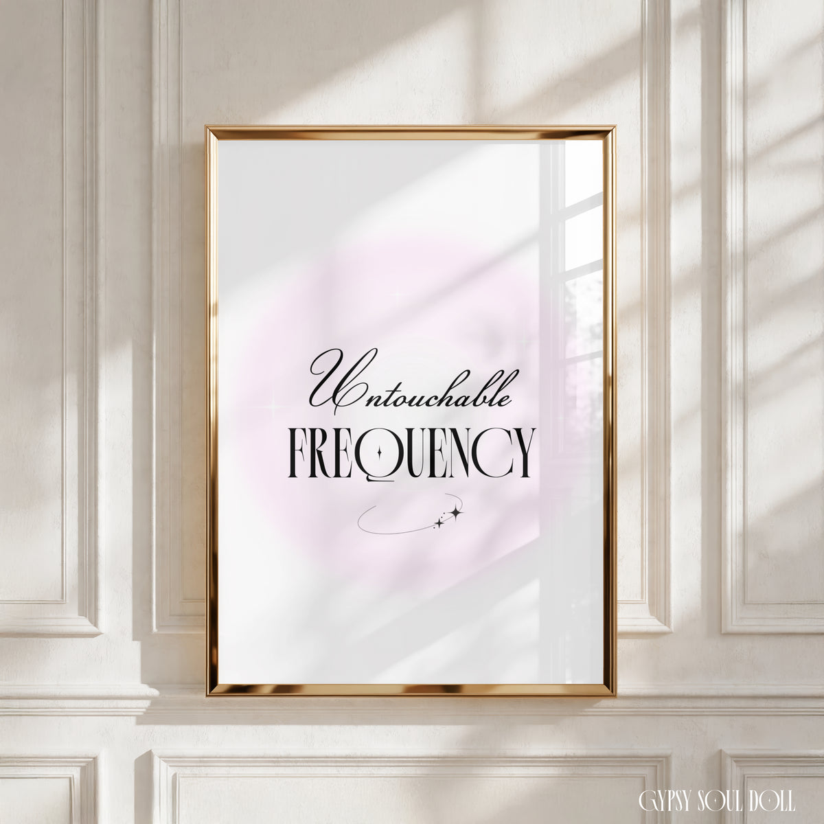 A framed typographic art print with the words 'Untouchable FREQUENCY' in black script and serif lettering over a soft pale pink circular backdrop, displayed on a white panelled wall with warm sunlight and window shadows by Gypsy Soul Doll.