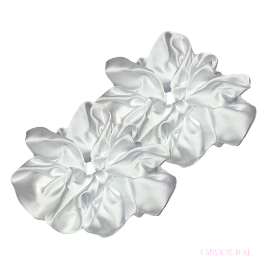 Two white satin hair scrunchies arranged diagonally on a plain white background.