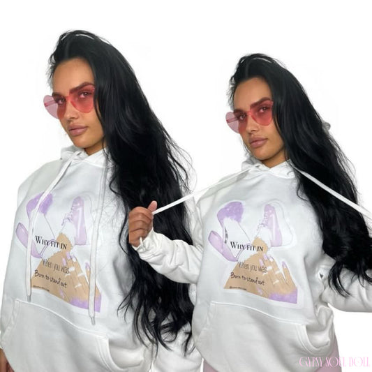 A woman modelling a white pullover hoodie with a graphic print on the front. The graphic features a purple and beige illustration and the text 'Why Fit In When You Was Born To Stand Out' and pink heart fashion glasses.