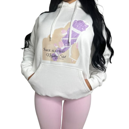 A woman wearing a white pullover hoodie with a graphic print on the front. The graphic features a hand with purple manicured nails and the text 'SAGE ALL THAT Negative Shit'.