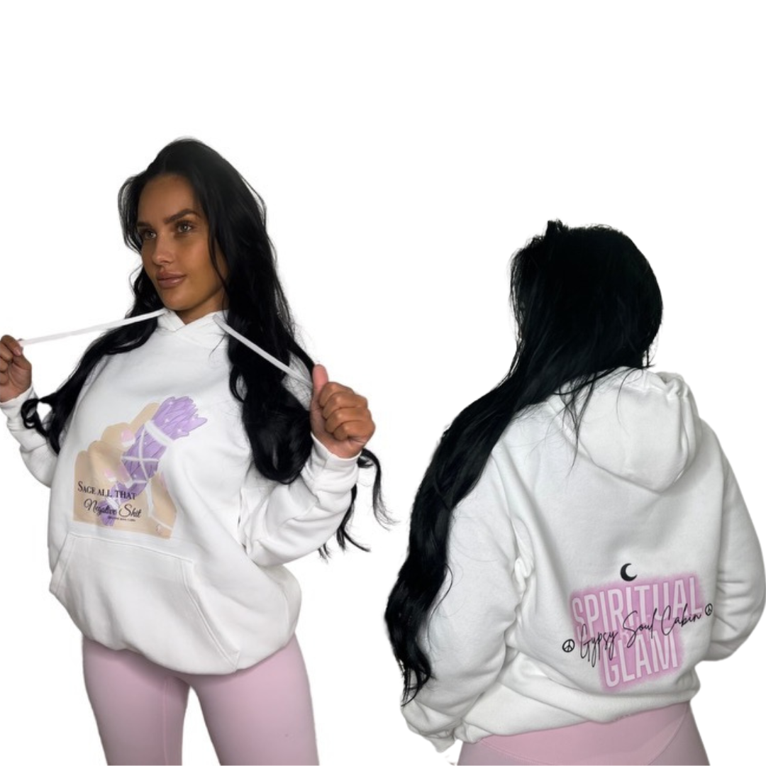 A woman modeling a white pullover hoodie shown from both front and back views against a plain white background. The front features a graphic with a hand holding a large sage and the text 'Sage all that negative shit', while the back displays a pink graphic reading 'SPIRITUAL BUT GLAM' with a small black crescent moon above it.