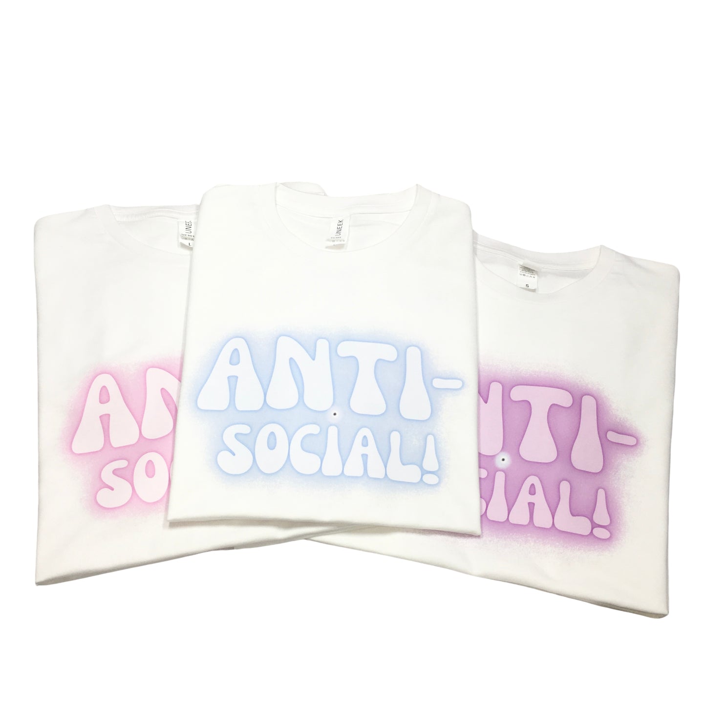 A trio of folded white streetwear graphic t-shirts stacked diagonally showing different pink, purple, and pastel blue fuzzy airbrush backdrop variations.