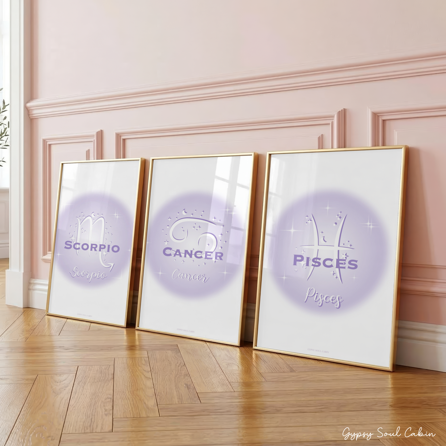 Three purple gradient aura zodiac prints featuring Scorpio, Cancer, and Pisces in large gold frames leaning against a classic panelled pink wall on a wooden herringbone floor.